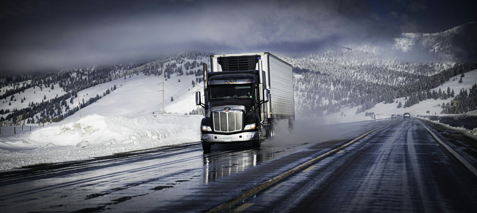 Tractor pulling a refrigerated trailer with its reefer unit visible, on a snowy highway